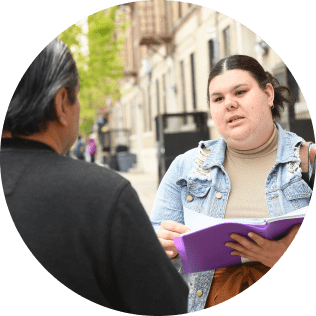 US staff member holding a binder in conversation with another adult on a New York City sidewalk