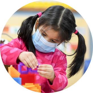 Young child with pigtails concentrating on building a structure with toy bricks