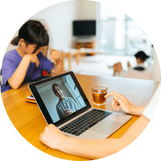 Laptop on a desk with a video call open in a living room with family in the background